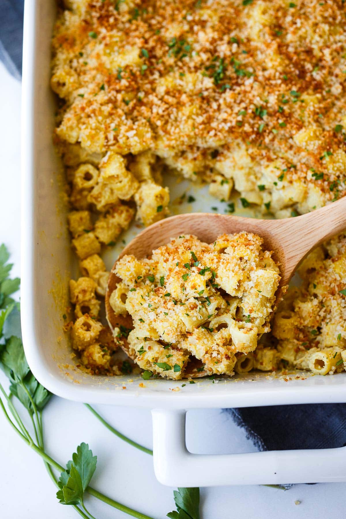 baking dish with baked vegan mac and cheese and wooden spoon scooping portion out. 