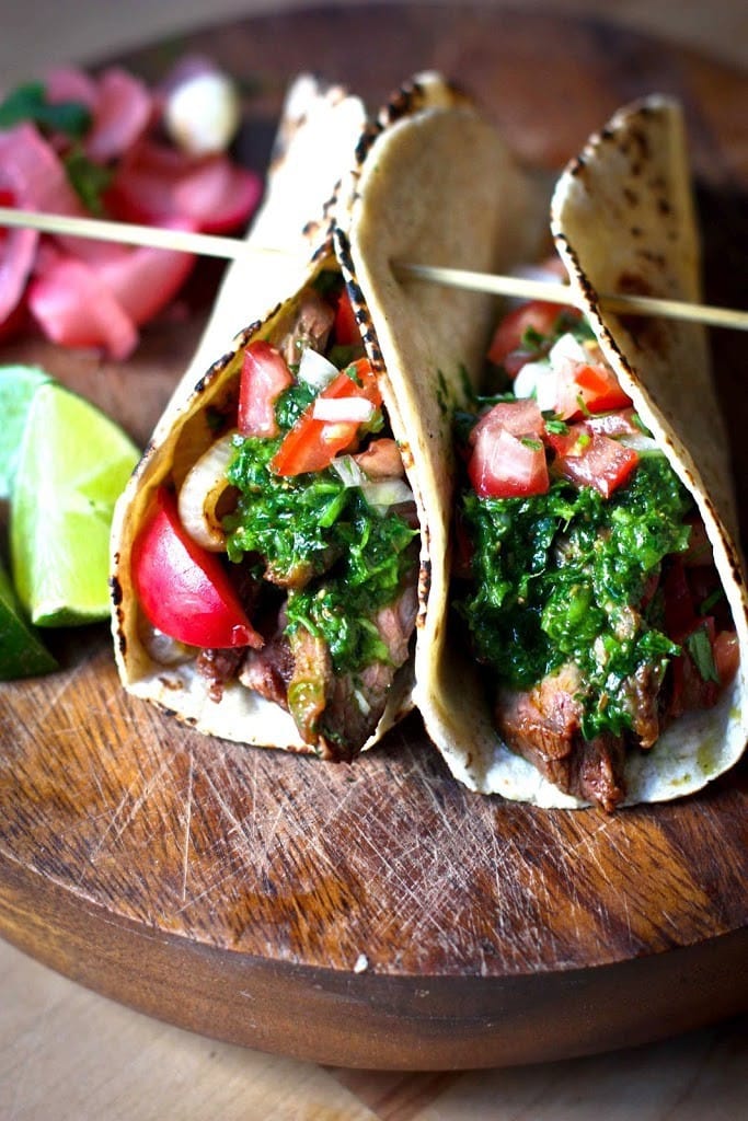 carne asada tacos topped with chimichurri sauce, pico de gallo, and pickled veggies, held together with toothpick.
