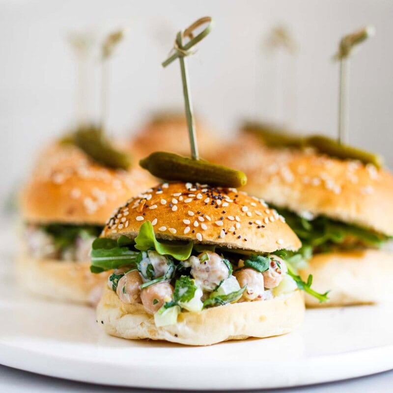 This Chickpea Salad Sandwich recipe is quick and easy- perfect for summer entertaining! We've used slider buns to turn them into an appetizer, topped with a cornichon pickle. Vegan-adaptable!