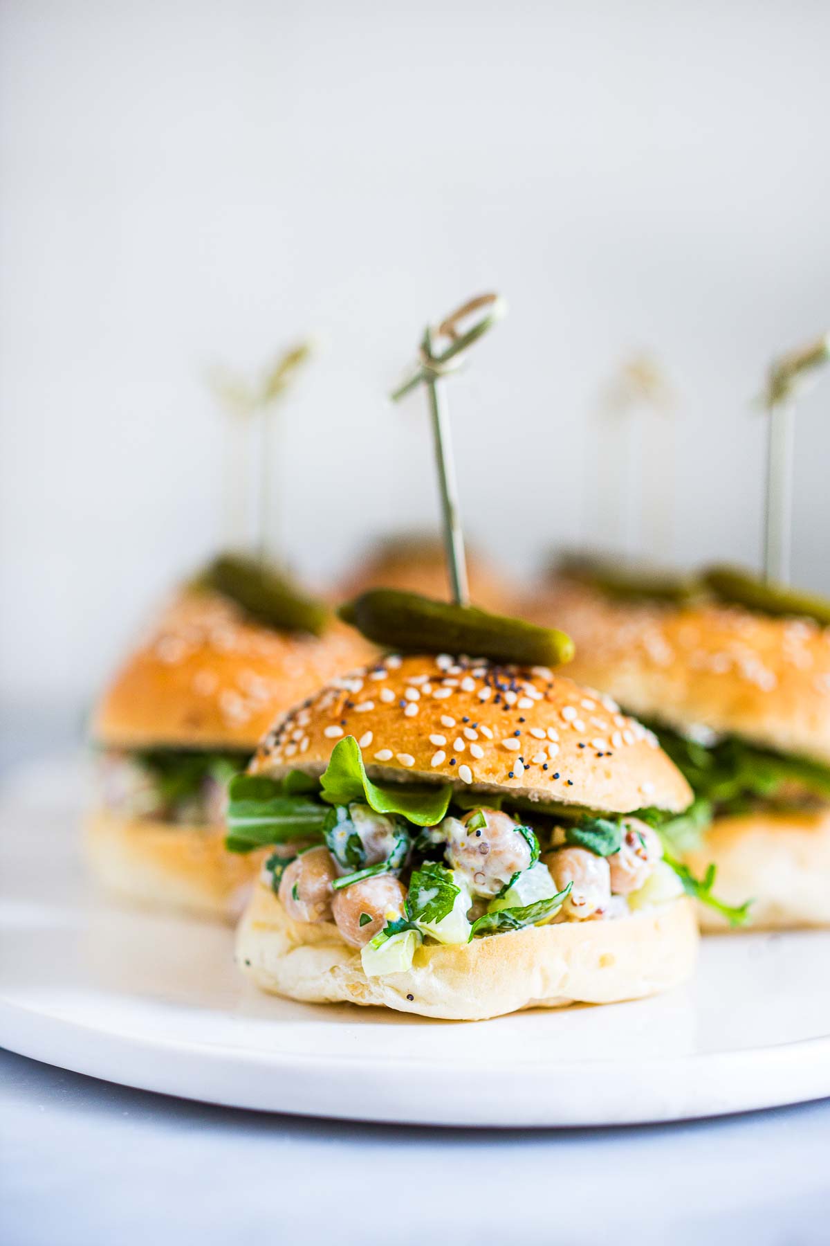 chickpea salad sandwich on slider bun, topped with cornichon on skewer.