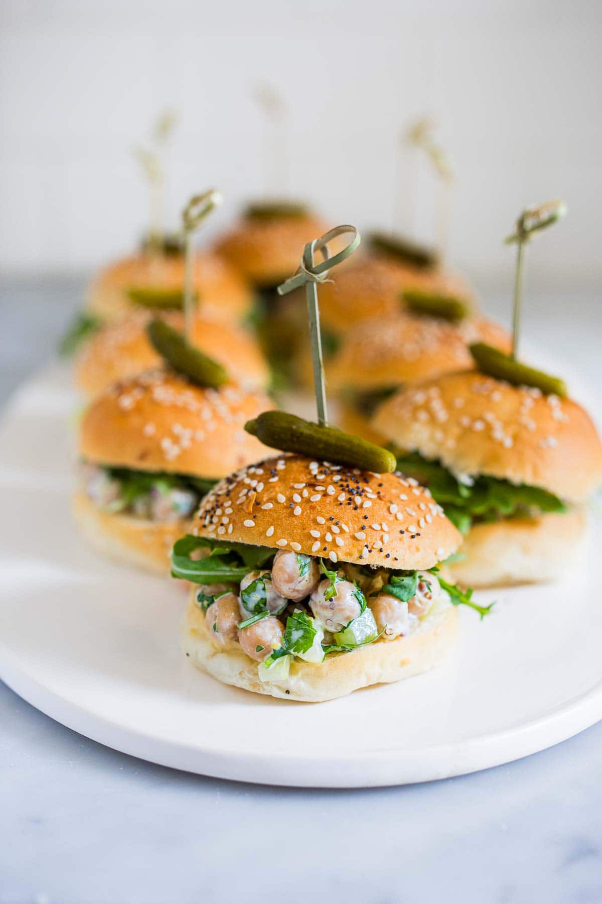 serving platter with chickpea salad sliders topped with cornichons on a skewer. 