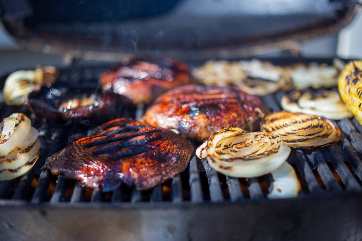 portobello mushrooms on the grill with slices of grilled onion and corn.