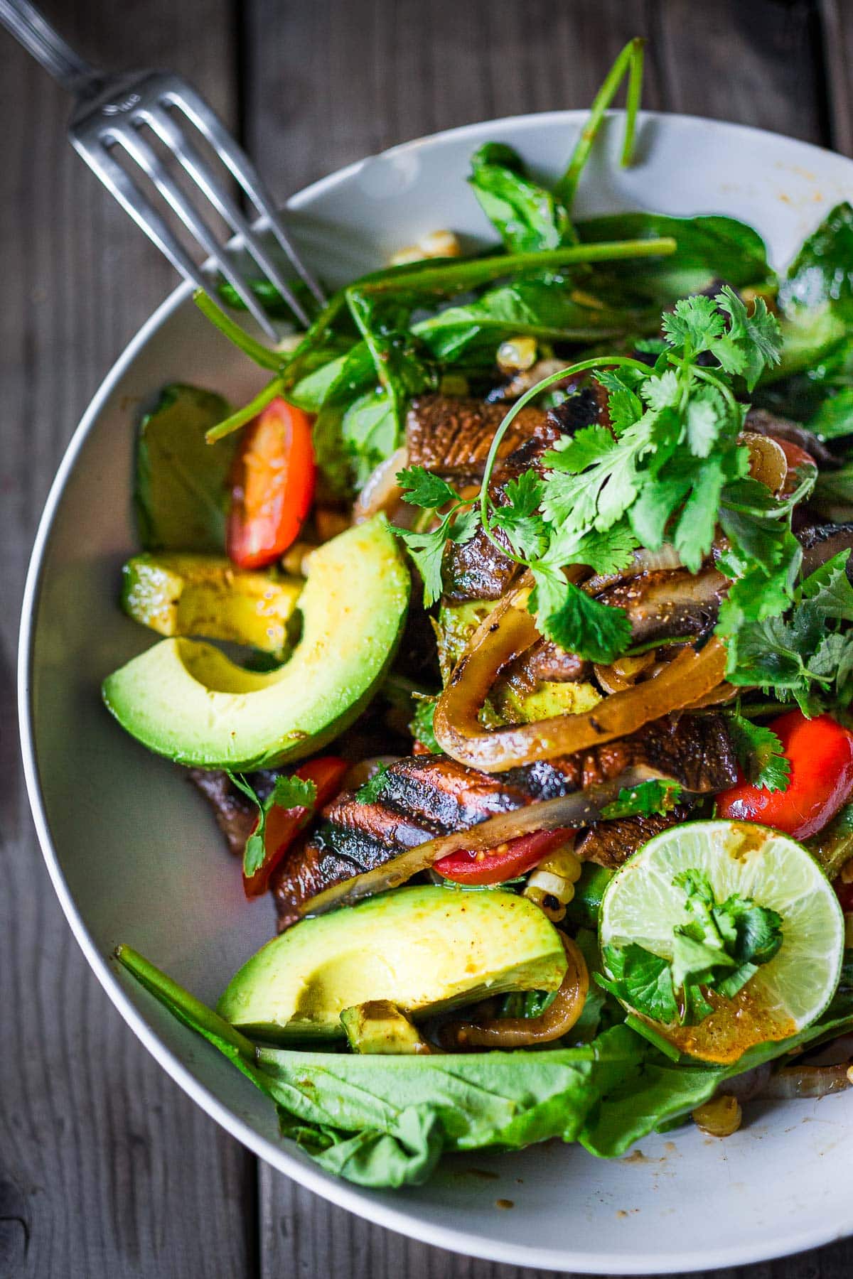 a bowl or salad with grilled portobello mushroom salad topped with fresh avocado and cherry tomatoes, grilled corn, and cilantro.