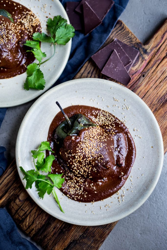 stuffed poblano pepper topped with mole negro sauce and toasted sesame seeds, served on plate with cilantro garnish.