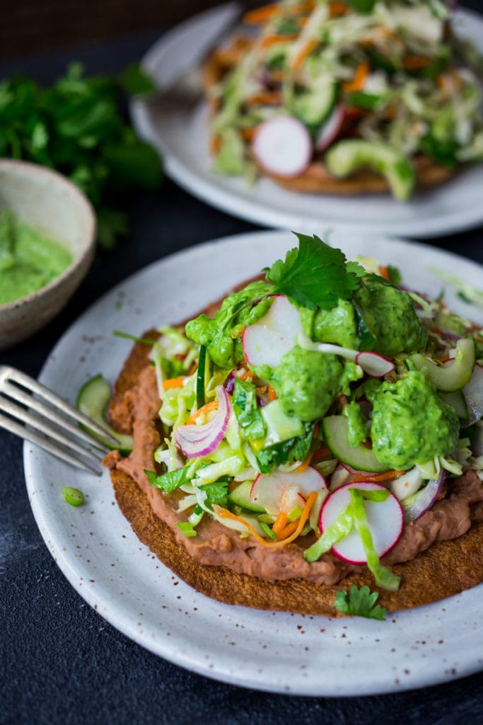 tlayuda on plate topped with refried beans, crunchy cabbage slaw, avocado sauce, and fresh cilantro.