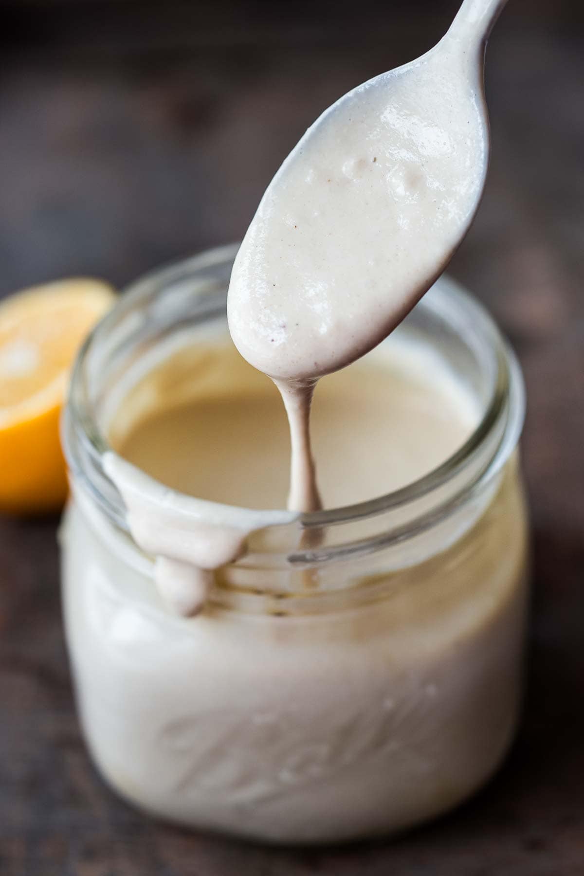 Tahini sauce in a jar with a spoon full of sauce. 