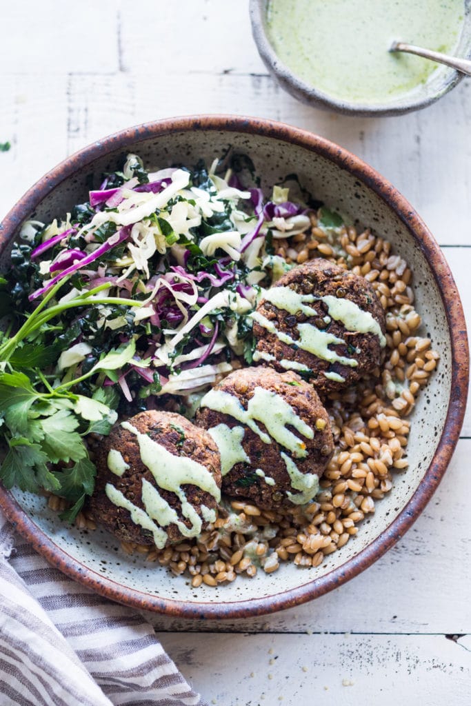 lentil patties on bed of whole grains, drizzled with zhoug sauce and served with kale cabbage slaw and herbs.
