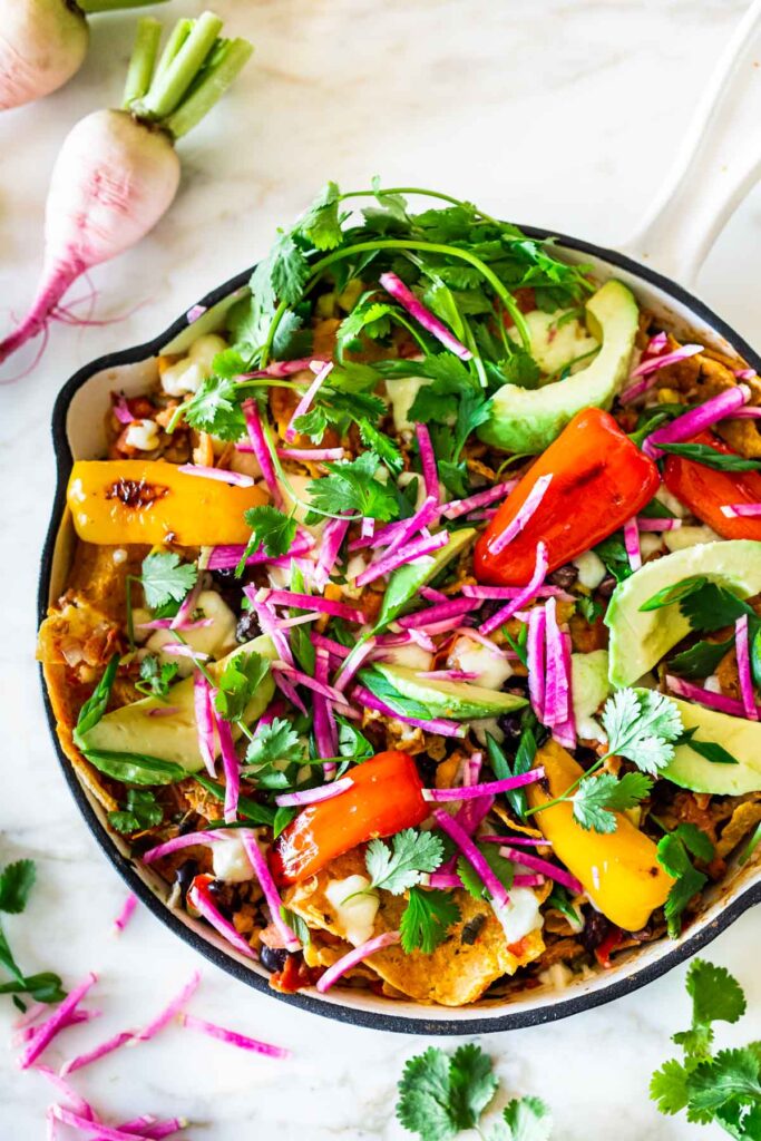 skillet with chilaquiles, topped with watermelon radish, sweet peppers, avocado, and cilantro.