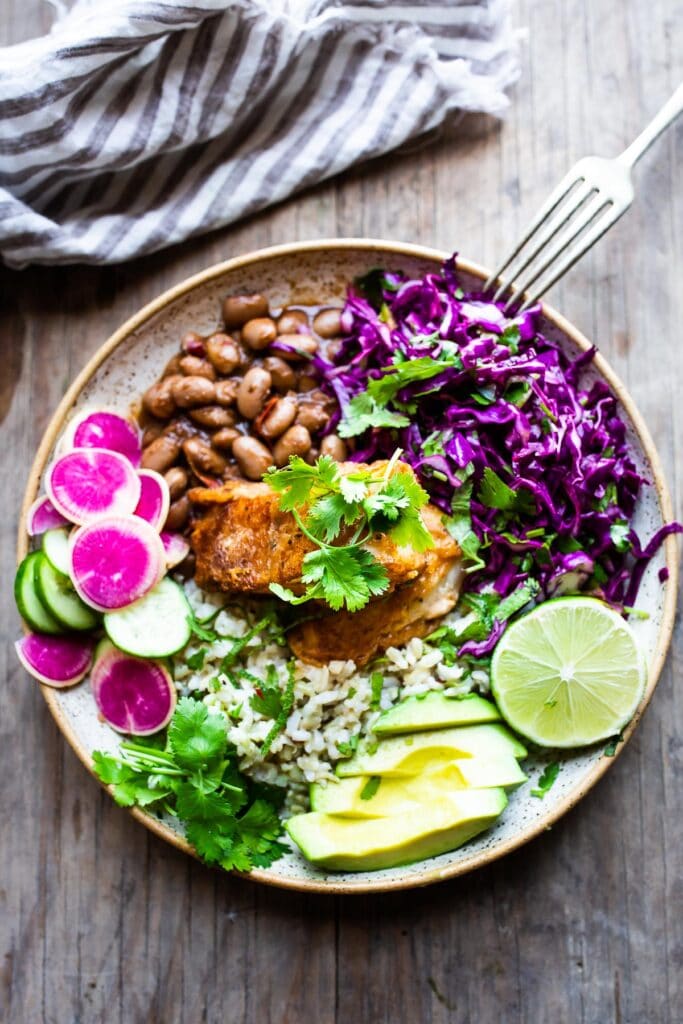 Baja fish taco bowl with rice, cabbage slaw, watermelon radish and cucumber, pinto beans, avocado, lime, and cilantro, topped with beer-battered cod.