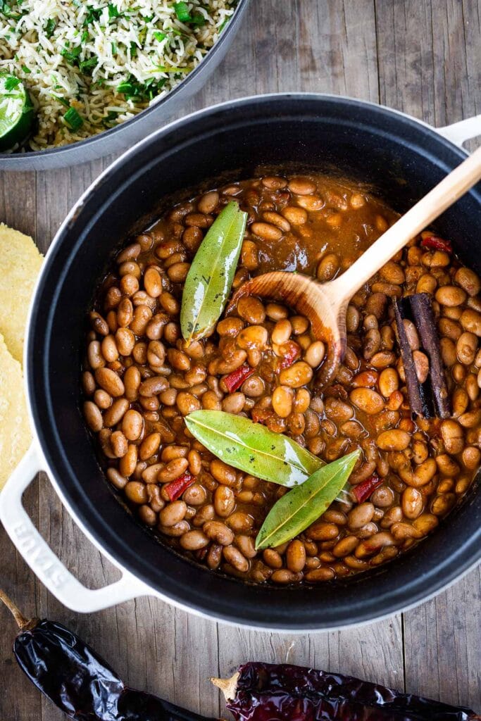 Dutch oven with homemade Mexican pinto beans, topped with bay leaves, red chiles, and cinnamon stick.
