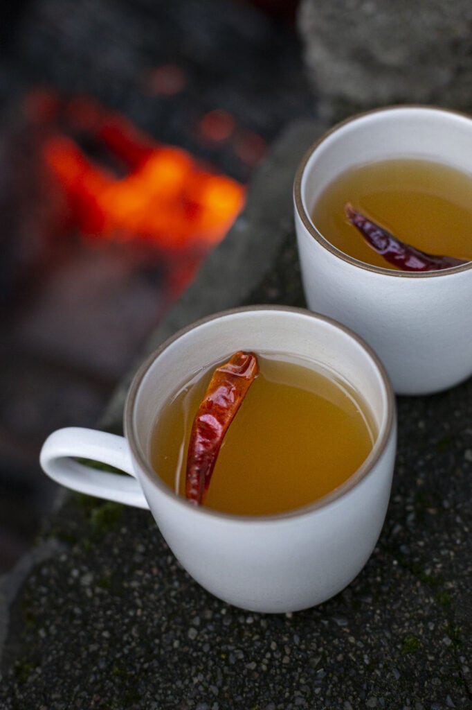 two mugs of Oaxacan hot toddy with a red chile garnish.