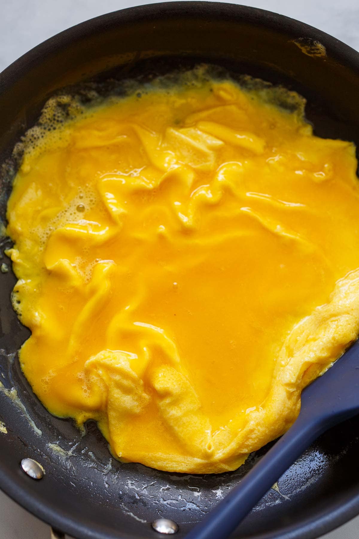omelette cooking in skillet with spatula pushing edges toward center.