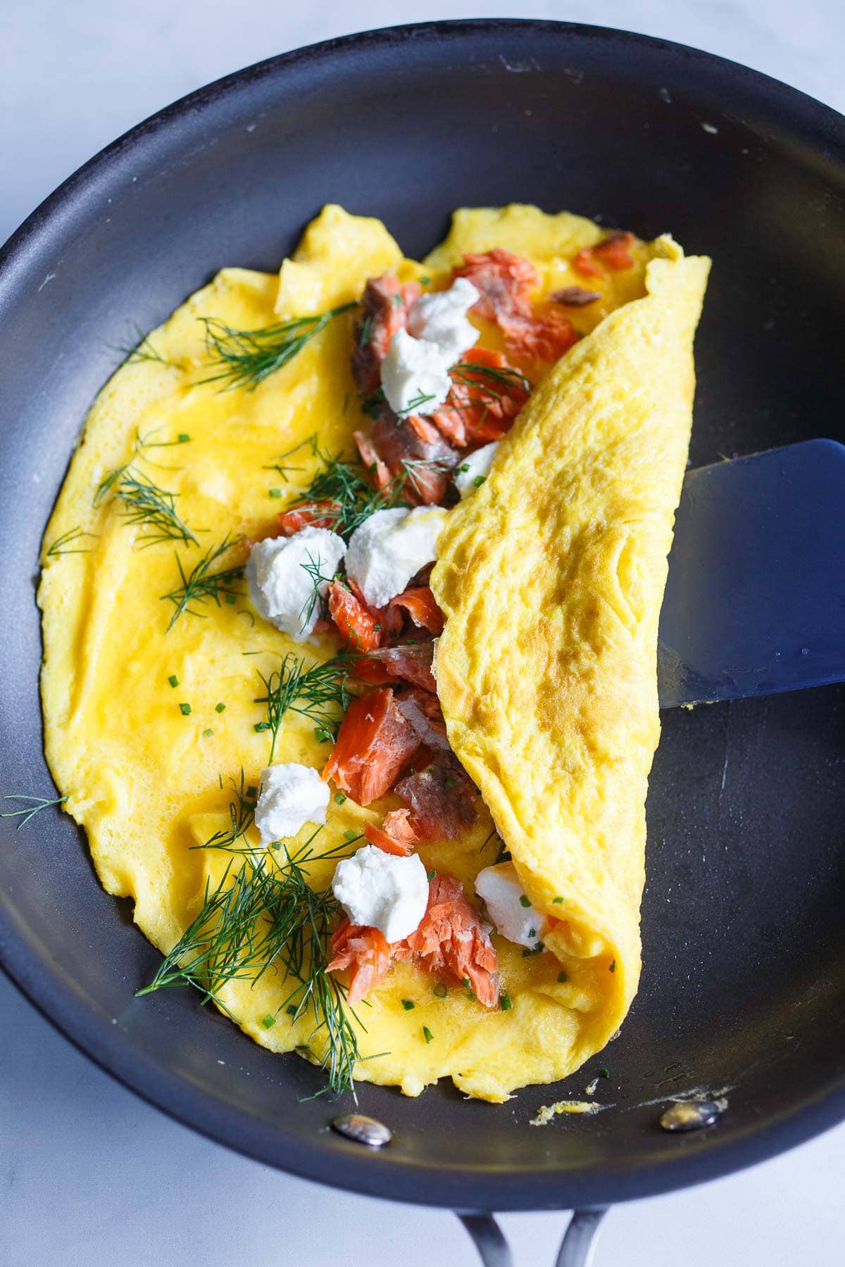 omelette in skillet, filling with salmon, herbs, and goat cheese, one fold over center.