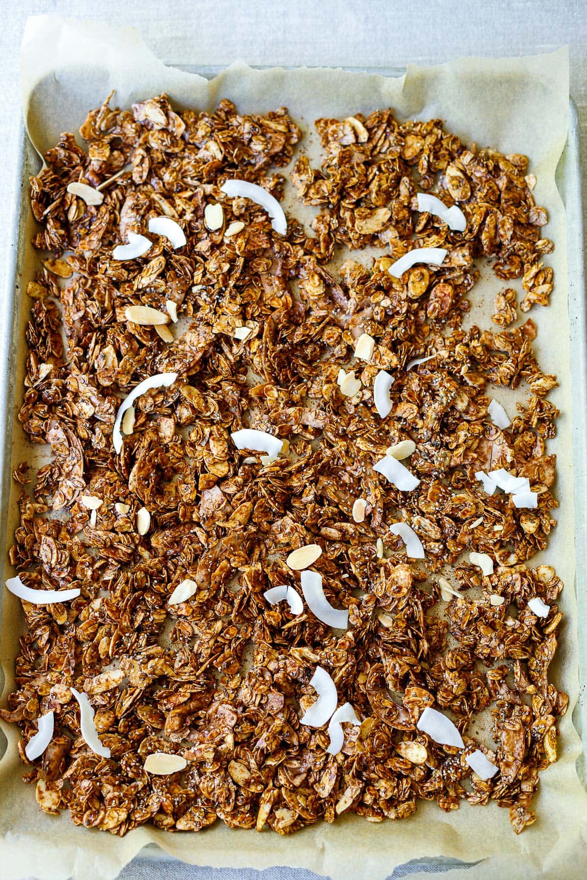 parchment-lined baking sheet with unbaked dark chocolate granola ingredients spread out. 