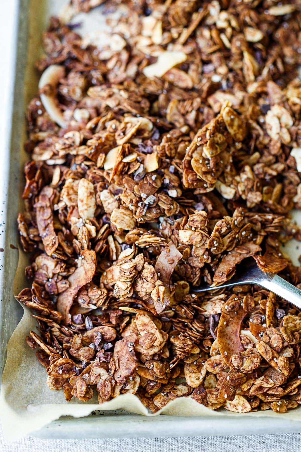 parchment-lined baking sheet with dark chocolate granola and spoon gathering a scoop. 