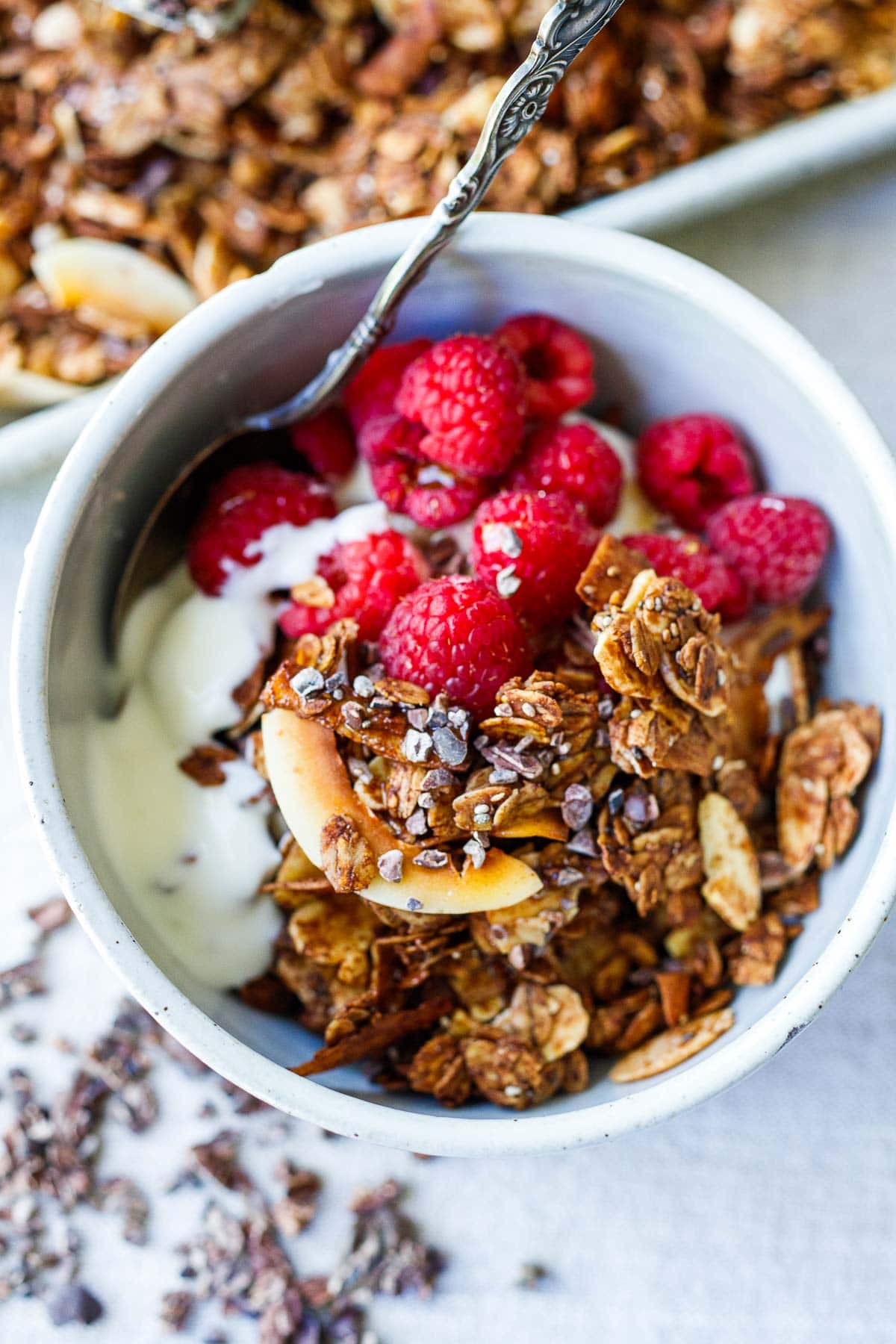 small bowl with yogurt, raspberries, and homemade dark chocolate granola with coconut flakes and cacao nibs. 