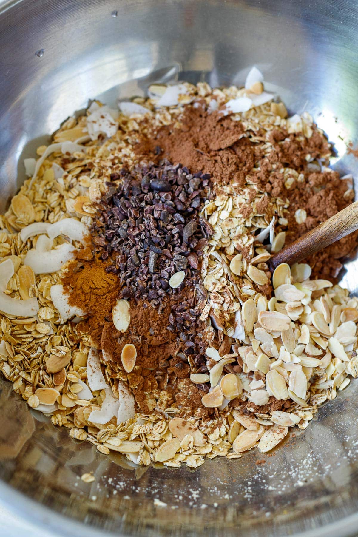 mixing bowl with rolled oats, cinnamon, cacao powder, cacao nibs, coconut flakes. 