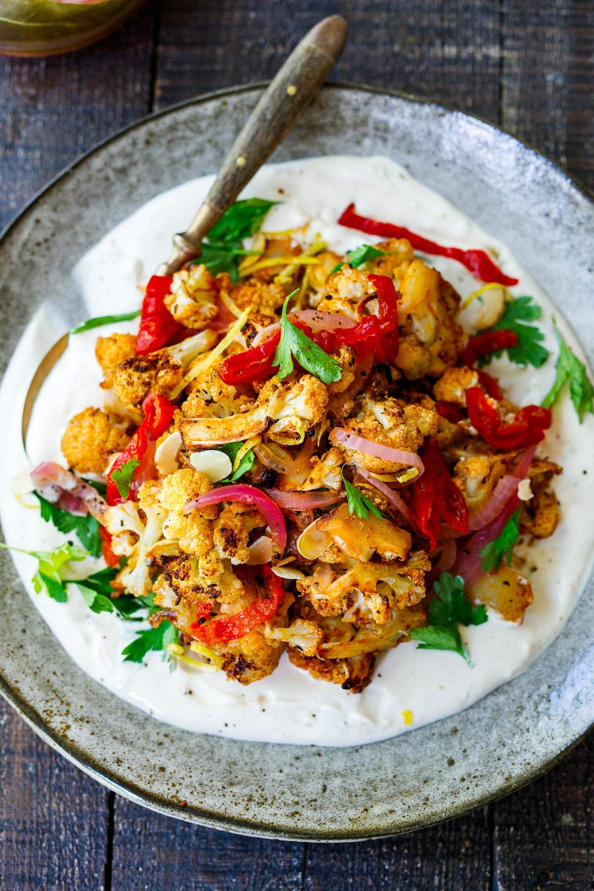 crispy cauliflower garnished with fresh parsley and lemon zest, pickled onions, piquant peppers, and slivered almonds, served over tahini yogurt. 