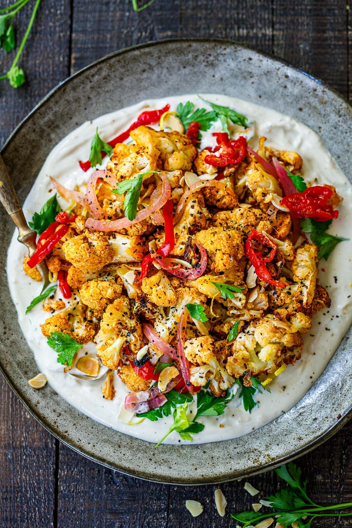 air fryer crispy cauliflower with pickled onions and piquant peppers served over tahini yogurt sauce on plate.