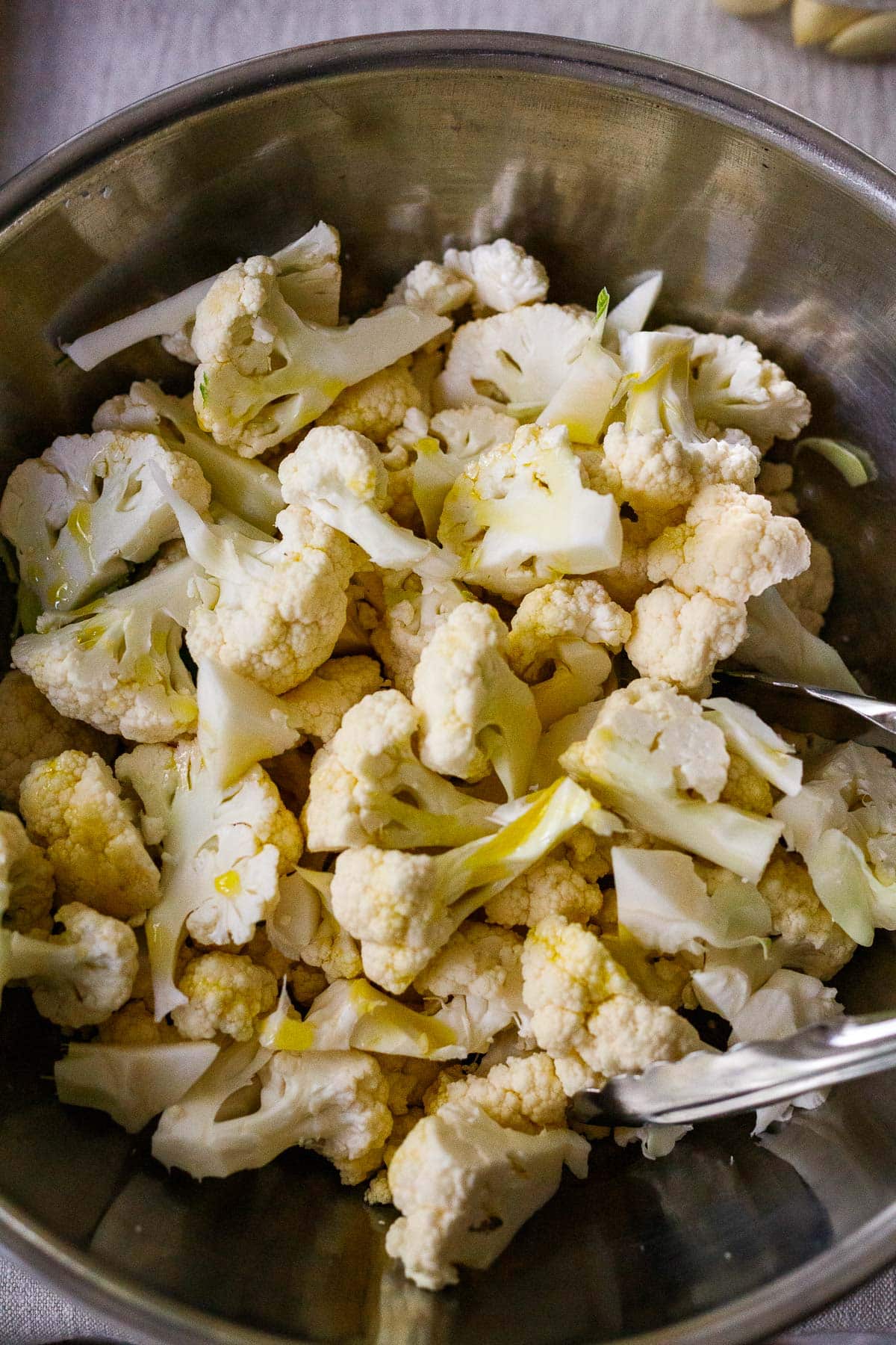 cauliflower florets in mixing bowl with oil drizzled over top.