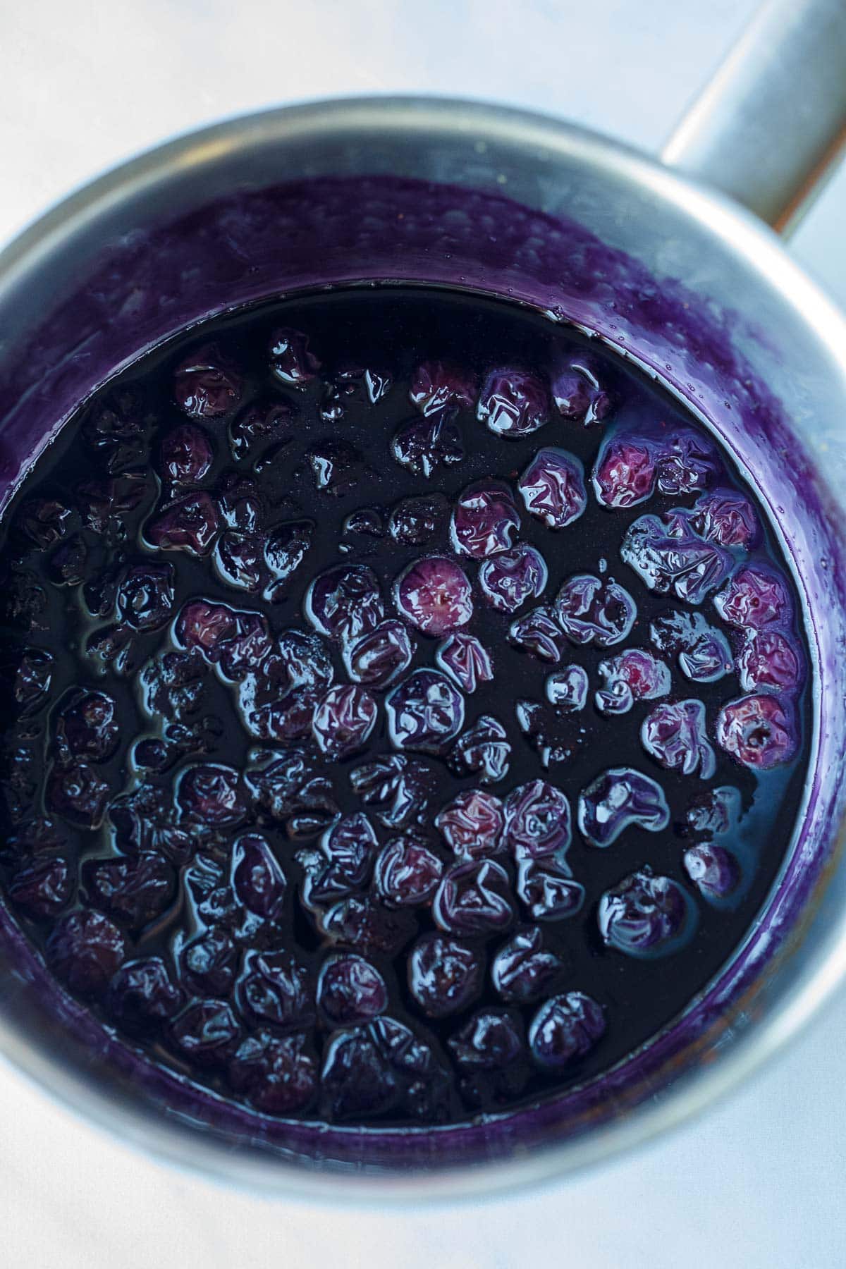 blueberry maple syrup simmering in saucepan with wilted berries.