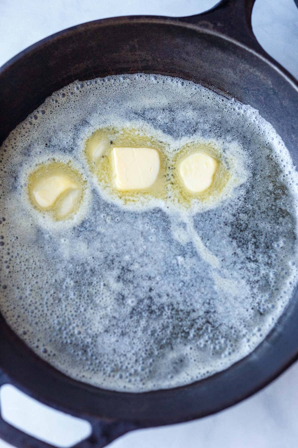 three pats of butter melting and spread out in hot cast iron skillet.