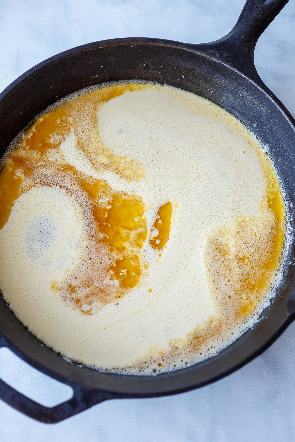 cast iron skillet with dutch baby batter spread out in pan.