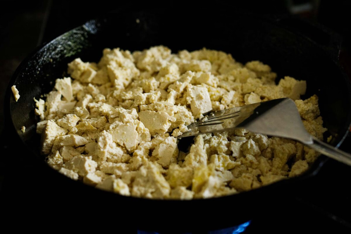 Breaking up tofu in a skillet.