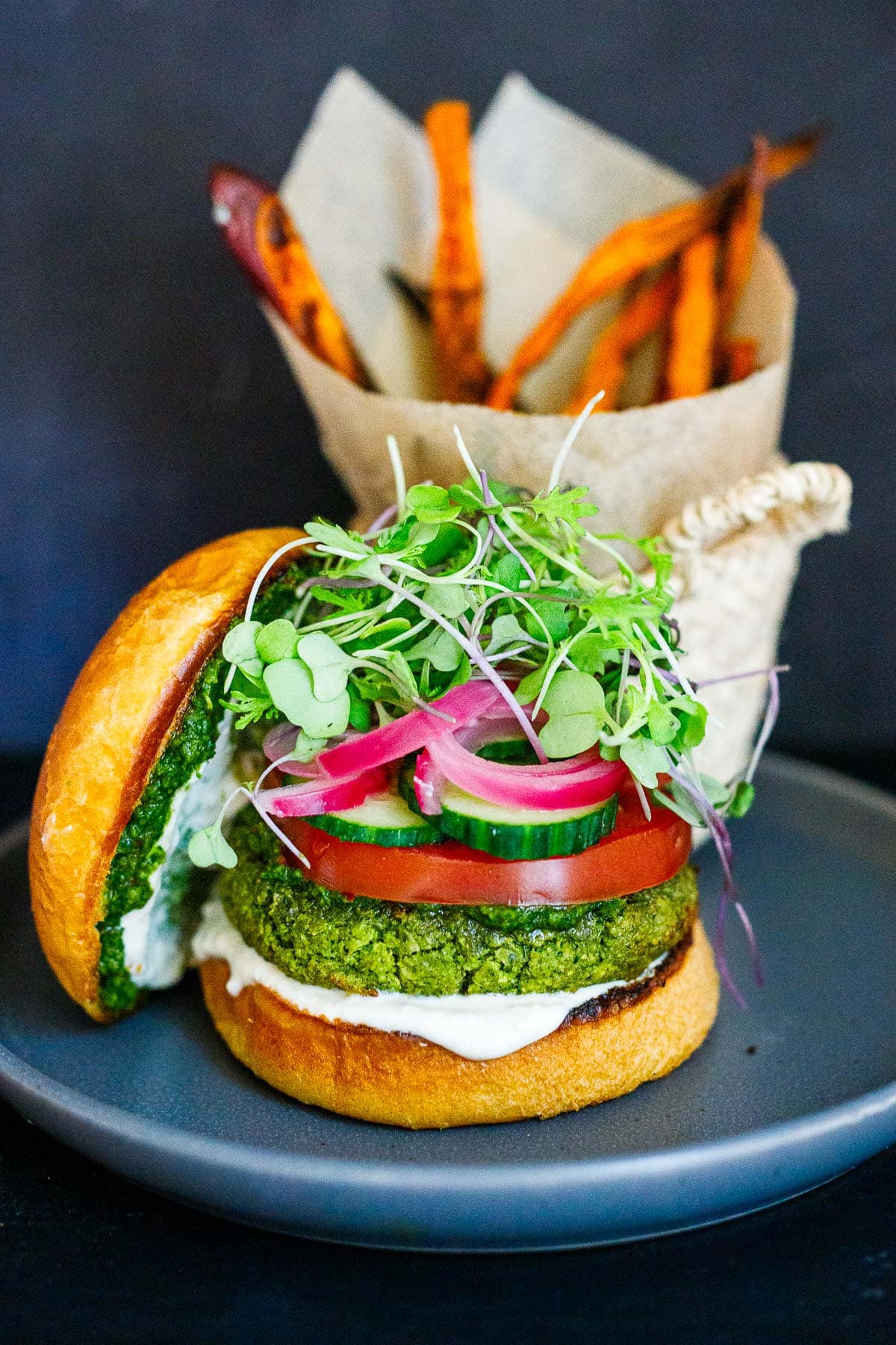 This falafel burger is a punchy, flavorful, high-protein vegetarian dinner! Top with tahini yogurt, pickled onions, sliced cucumbers, and tomatoes on a toasty brioche bun.