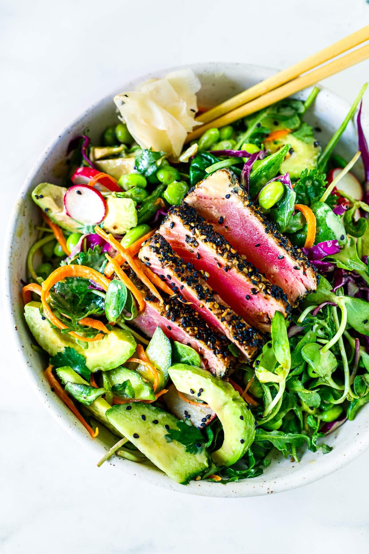 This sesame-crusted seared ahi tuna salad recipe is deliciously refreshing and light! Served over fresh greens with avocado, cucumber, edamame, grated carrots, cabbage, radishes, and sunflower sprouts tossed in a ginger wasabi vinaigrette.